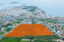 Foto aérea del ámbito de Ca N'Escandell. En primer plano aparece una zona sin urbanizar resaltada con un color naranja, al fondo se ve la ciudad de Ibiza y el mar.